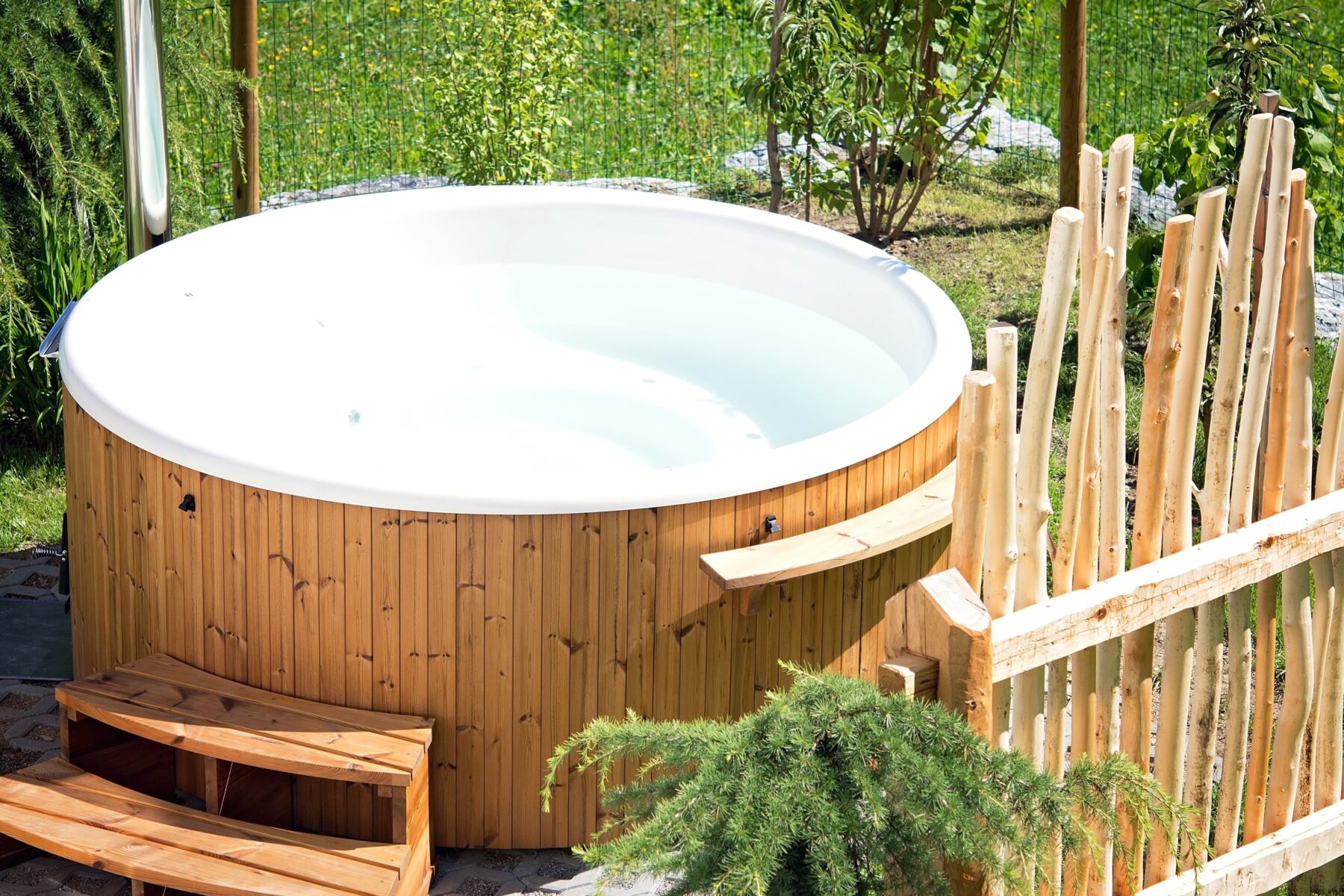 Spa hors-sol extérieur en bois. Il y'a une barrière en bois qui cache le spa pour l'intimité des baigneurs.