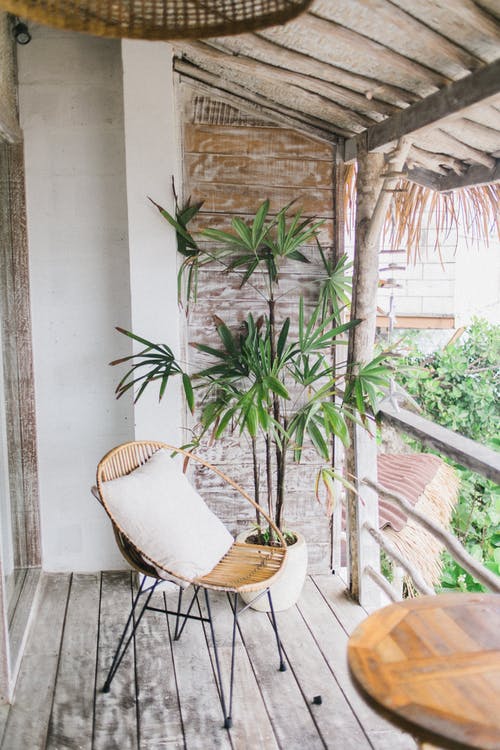 Balcon aménagé avec une chaise en rotin et une plante en fond.