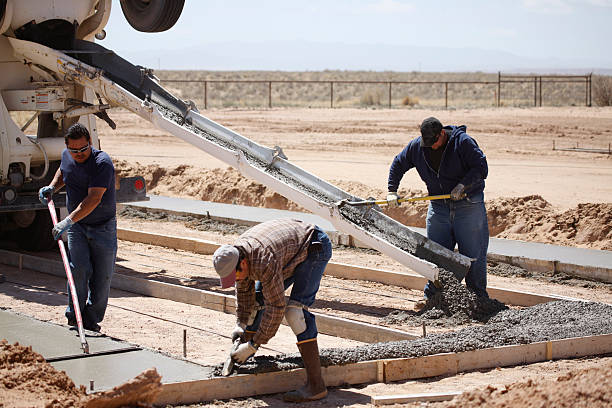 Trois hommes travaillant sur une dalle de béton pour une fondation de maison.