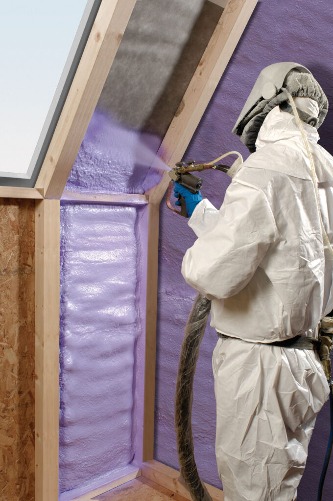 pour une isolation de plafond en appartement par projection de mousse, un ouvrier en tenue protectrice projette un matériau mousse violet dans une toiture