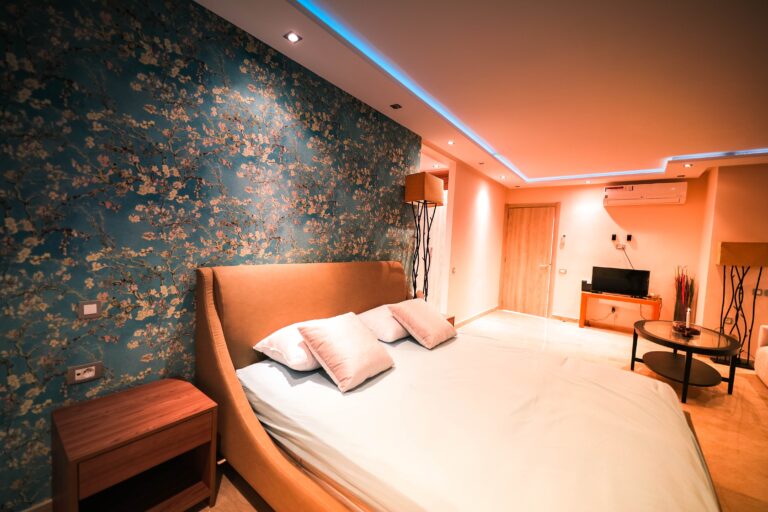 Une vaste chambre à coucher à l'ameublement épuré, avec un lit appuyé sur un mur en papier peint bleu à motifs floraux.