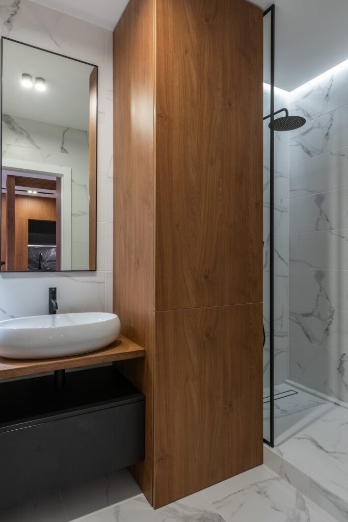 exemple de rénovation de salle de bain en appartement avec une cabine de douche à vitres, carrelage marbre et mobilier en bois