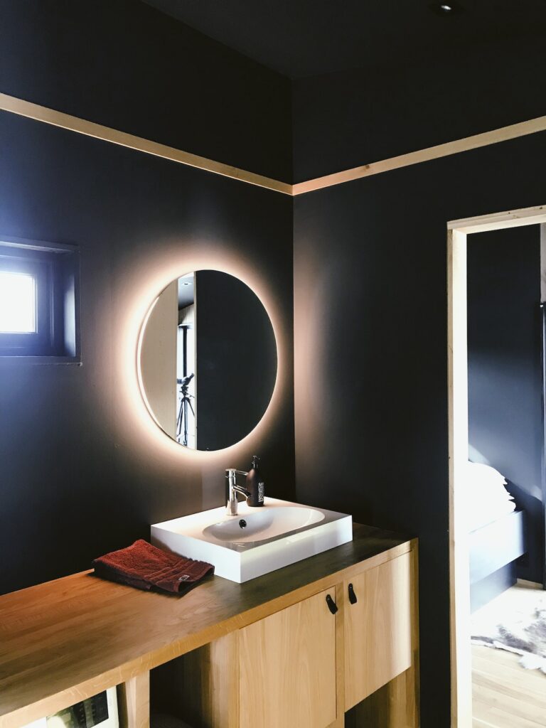 exemple de rénovation de salle de bain en appartement avec miroir rétroéclairé, murs noirs et meuble en bois