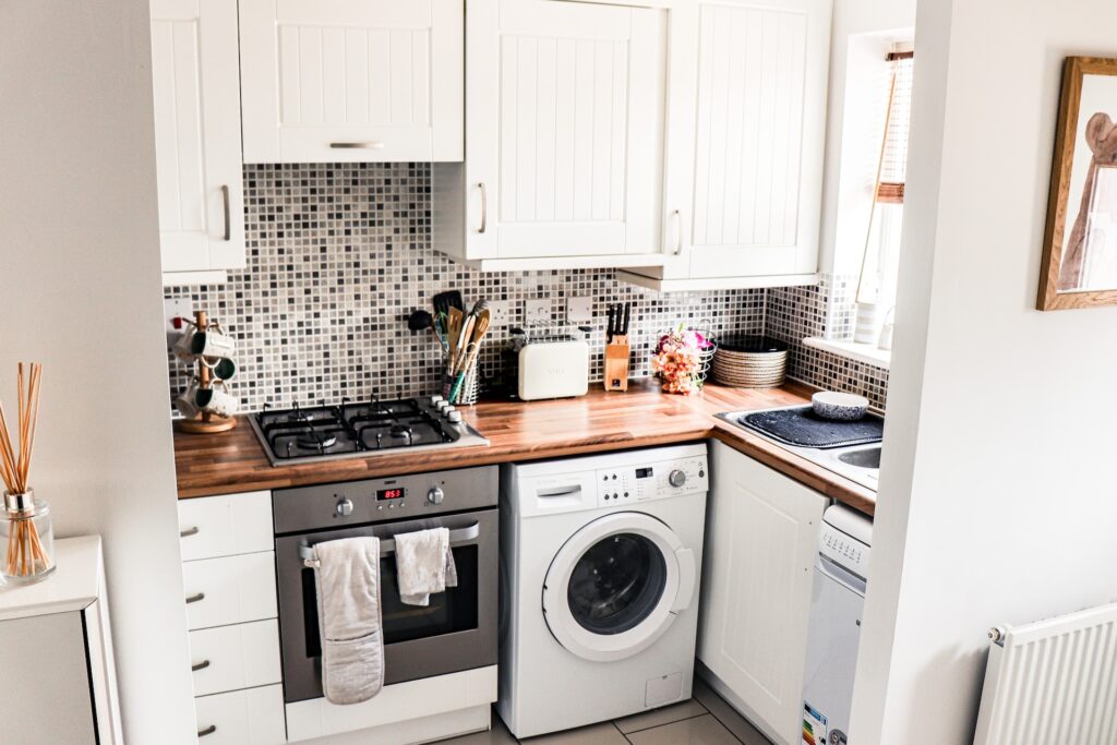 Espace cuisine blanc avec un évier, un four, une machine à laver et une plaque de gaz.