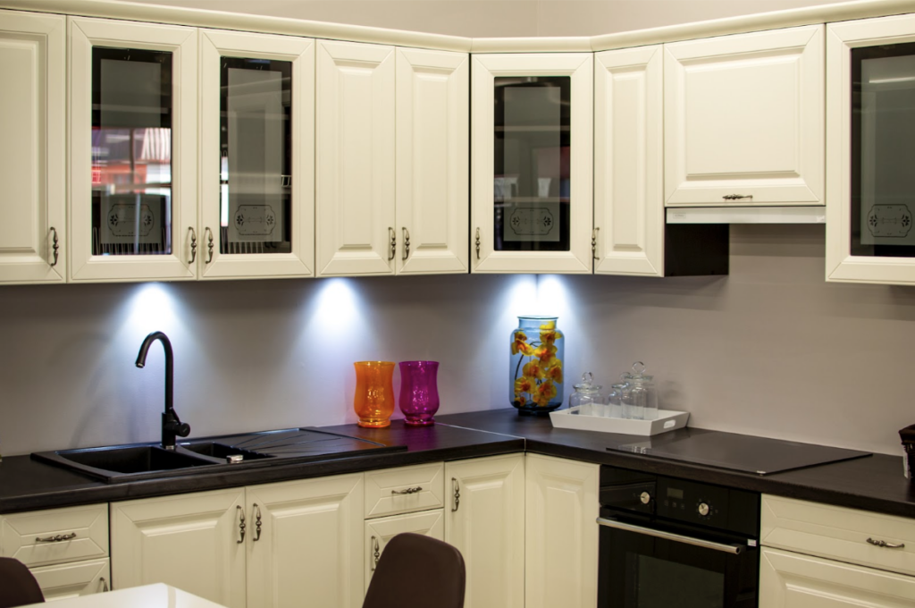 Pour aménager une petite cuisine fermée, il faut faire attention à l'utilisation de l'éclairage. En installant des lampes en dessous des meubles en hauteur contre les murs, la pièce est plus lumineuse et spacieuse. Ici, nous avons une petite cuisine fermée en L avec des couleurs contrastées en noir et blanc. Les lampes situées sous les meubles en hauteur offrent des rayons lumineux qui rendent la pièce spacieuse et moderne. La cuisine est fonctionnelle avec de nombreux appareils électroménagers et des produits alimentaires. Les meubles sont blancs avec quelques vitrines noires pour ceux en hauteur. Le plateau de cuisine est noir tout comme l'électroménager.