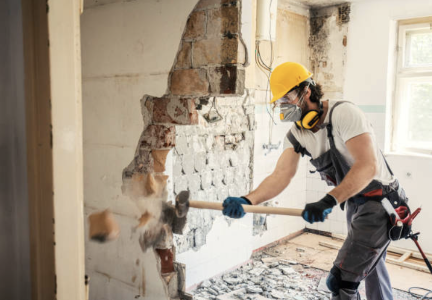 Un homme, masse à la main, frappe un mur. Extension dans le cadre entreprise rénovation