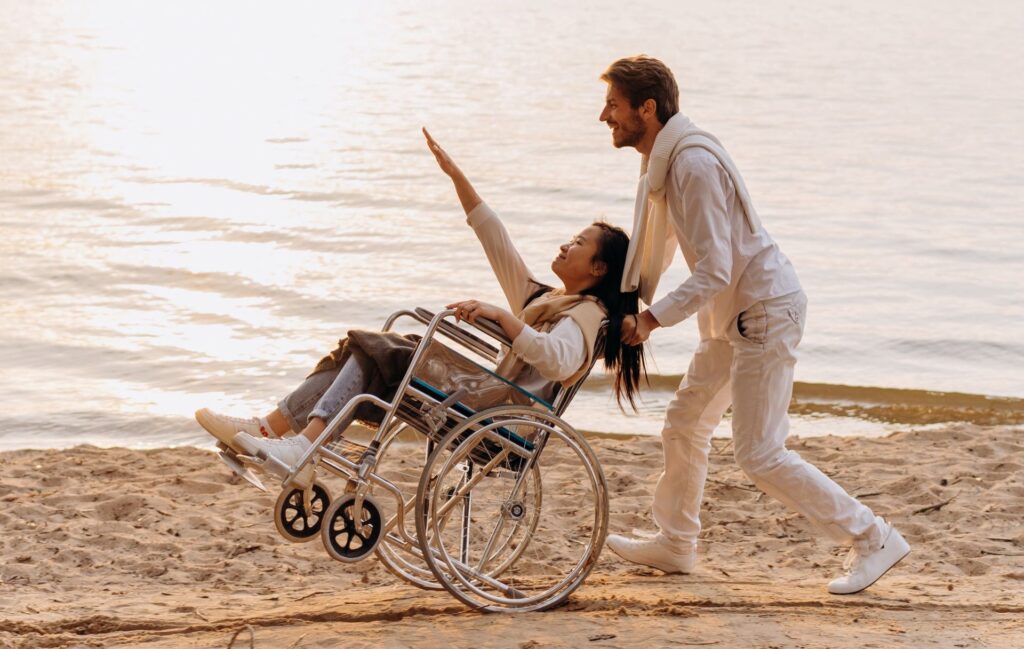 couple heureux habillé en blanc au bord de la mer au coucher du soleil avec femme en fauteuil roulant