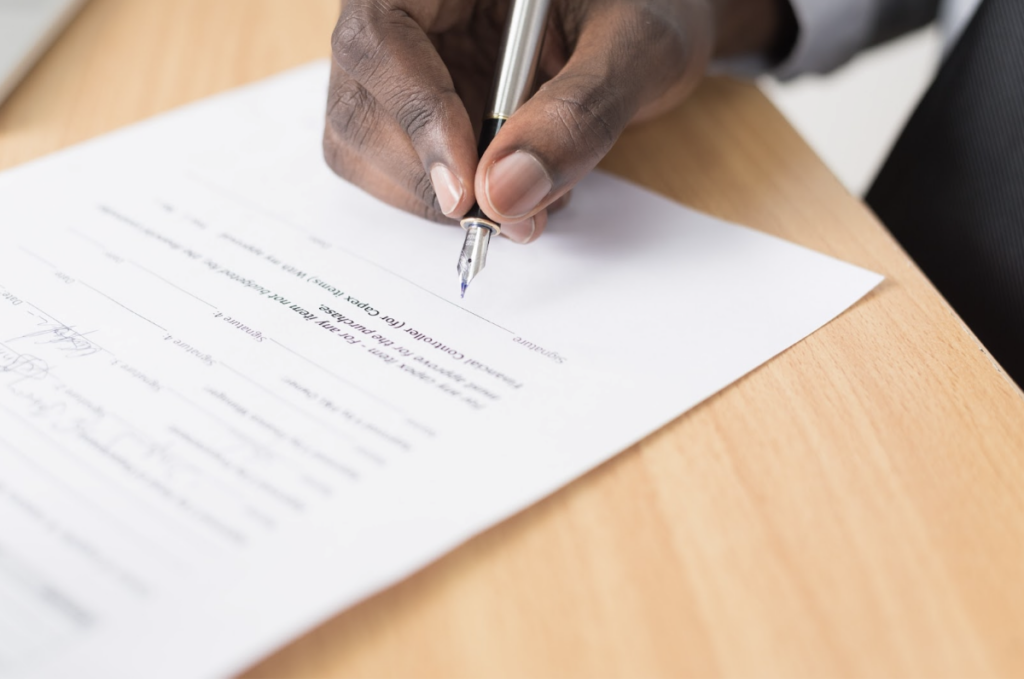 Individu en train de rédiger ou de compléter un contrat, stylo à la main sur une table en bois