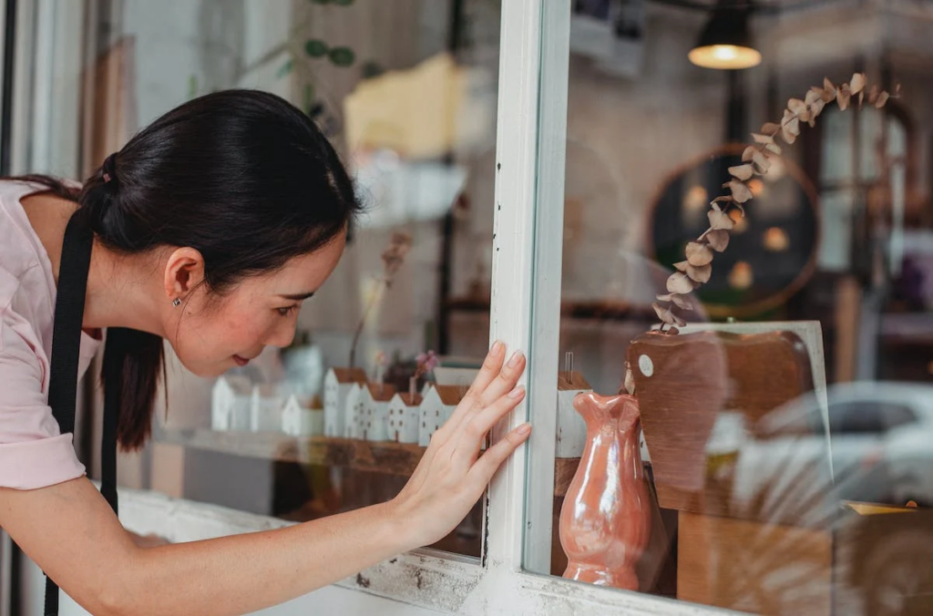 Une jeune femme observe un vase. Elle s'appuie avec sa main contre la paroi en verre pour mieux examiner un petit vase rose émaillé qui se trouve à l'intérieur.