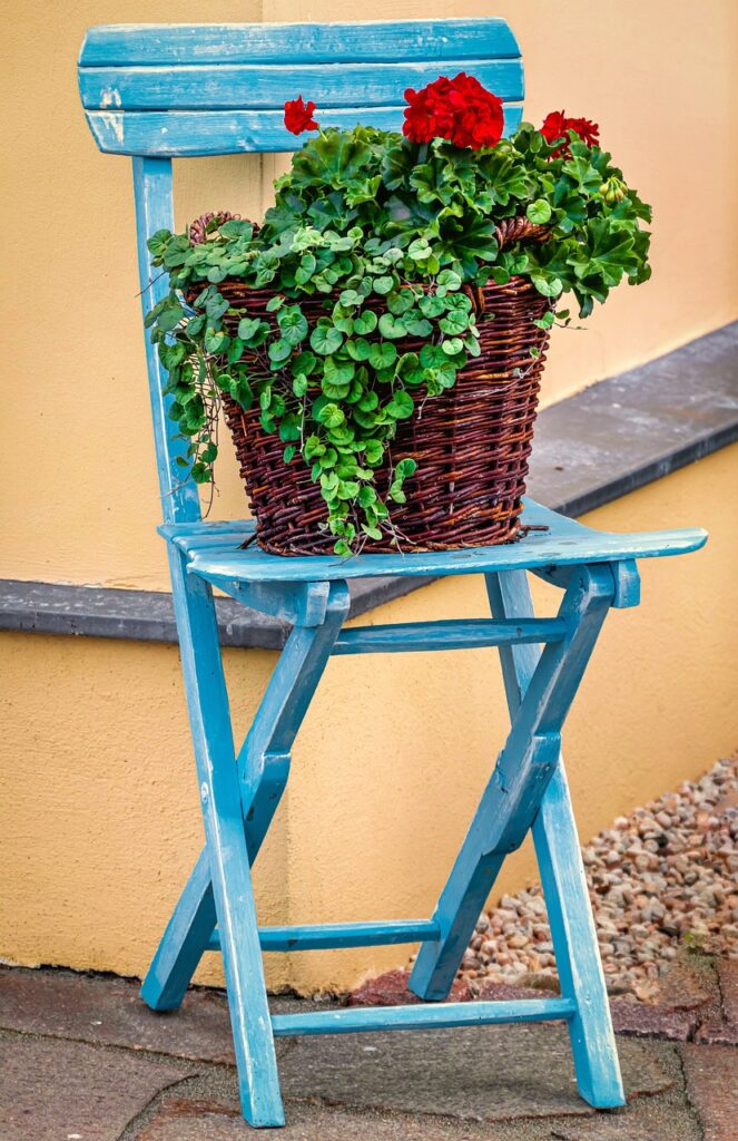 Idée de couleur meuble en bois peint en bleu. Une chaise se trouve dans la rue, sur laquelle on a disposer un pot de fleurs.