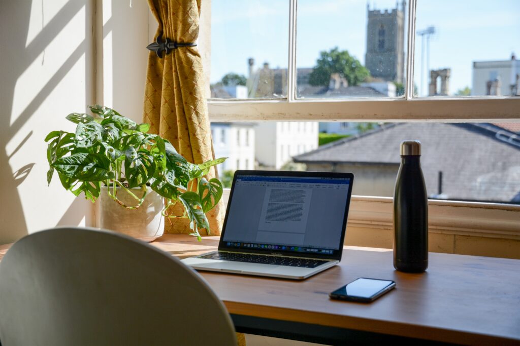 Bureau face à la fenêtre avec une plante en pot, un ordinateur portable et une gourde d'eau.