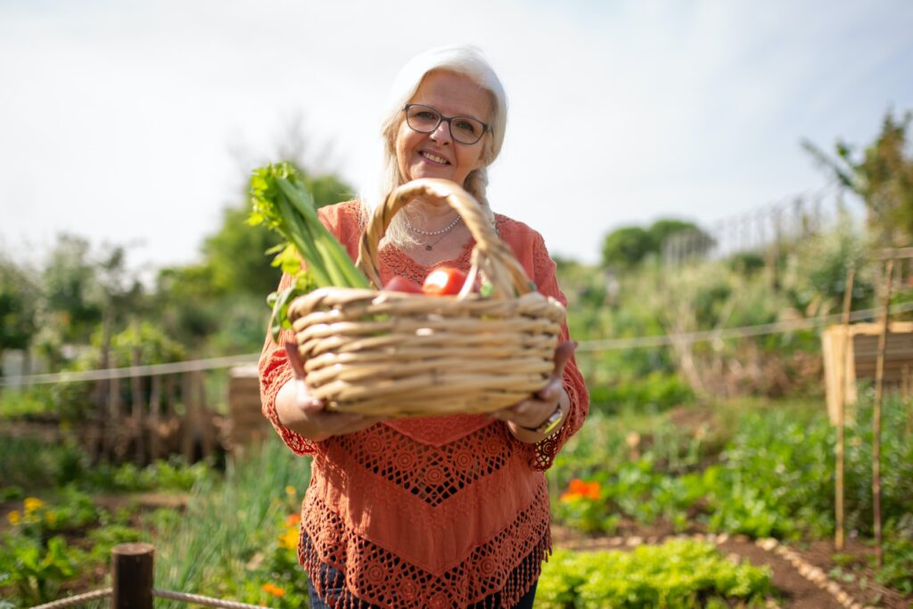 Femme tenant un panier rempli de légume dans un potager