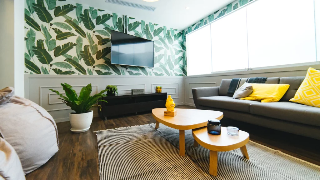 aménagement d'un sous-sol avec salon : tapis sol, canapé gris, deux petites tables basses et murs papier peint feuilles / vert