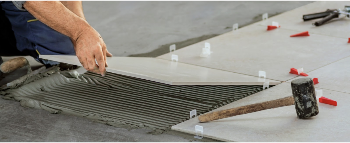 Un homme travaille sur un chantier. Il est en train de poser du carrelage à l'intérieur d'une pièce où une chape fluide est déjà posée.