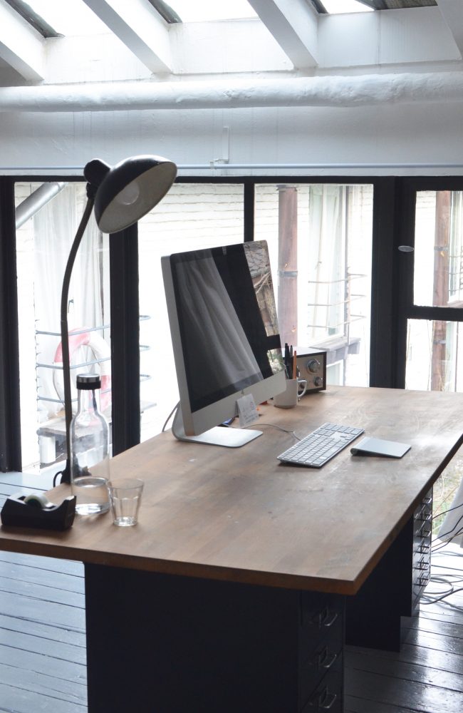 Bureau dans un style industriel avec un bureau en bois et métal. Sur le bureau se trouve un elampe en métal.