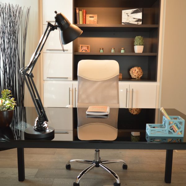 Bureau noir avec une fauteuil à roulettes blanc. Sur le bureau se trouve une grande lampe en métal.